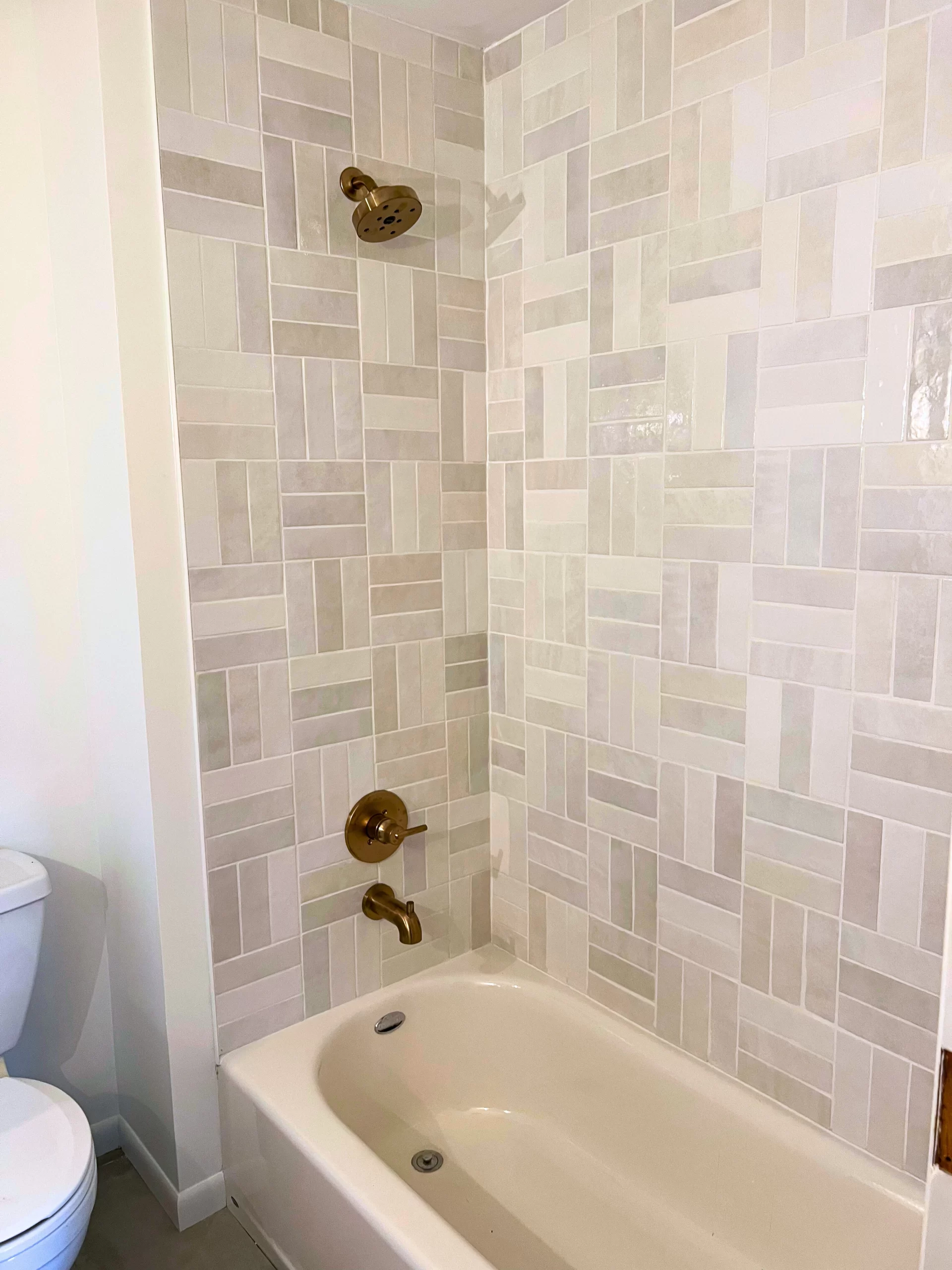 A shower featuring tile in shades of greige with gold fixtures